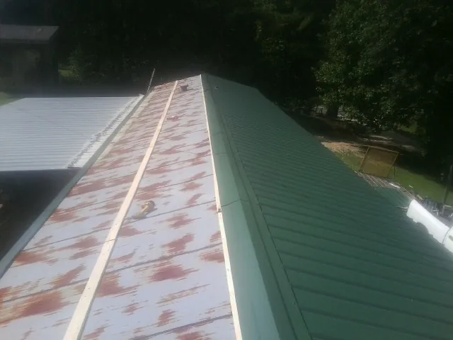 Old rusted panels beside newly installed green metal roofing in Fishers