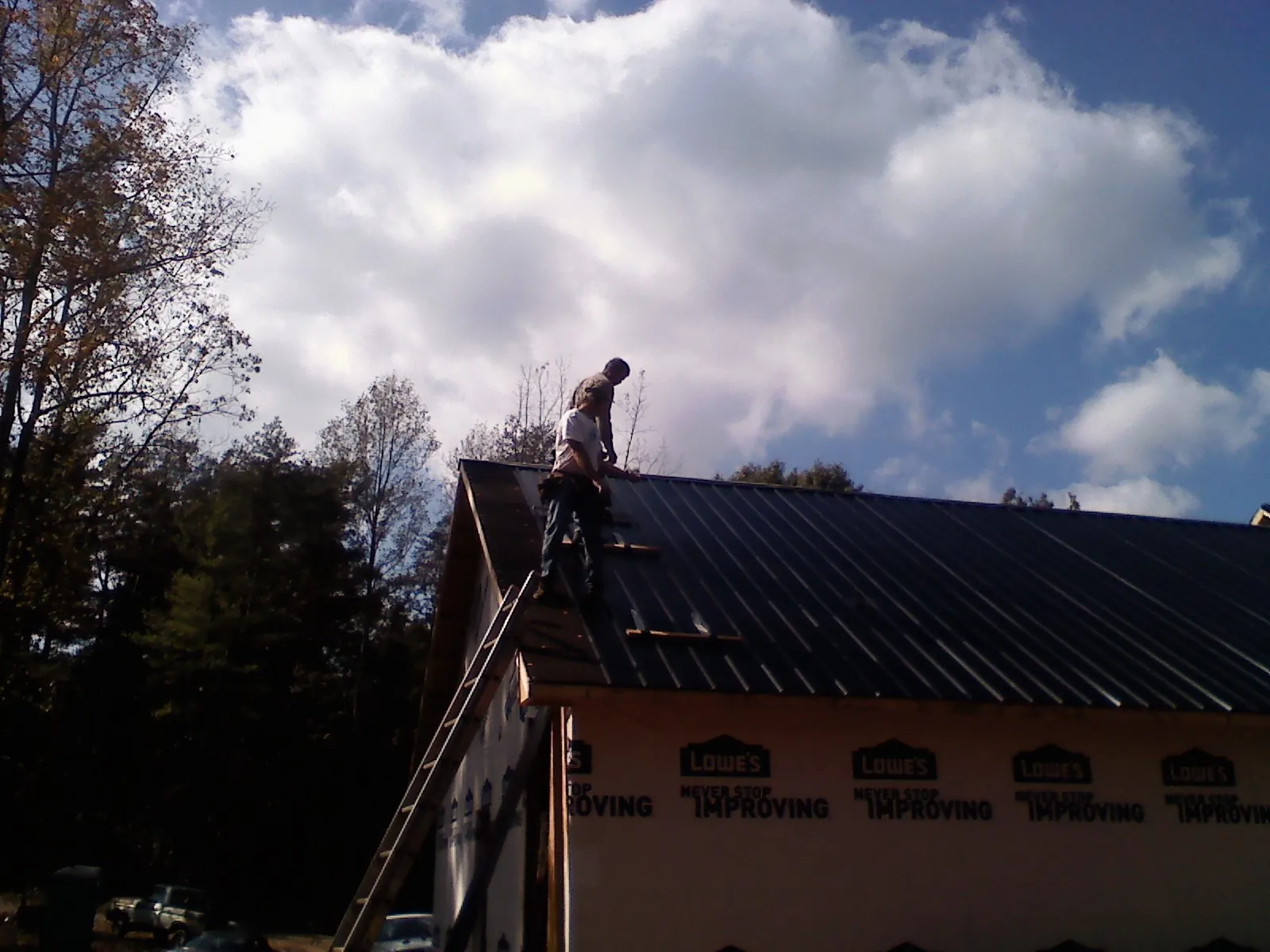 Roofer fastening dark metal panels high against a cloudy sky, from a Roof Inspection job in Fishers
