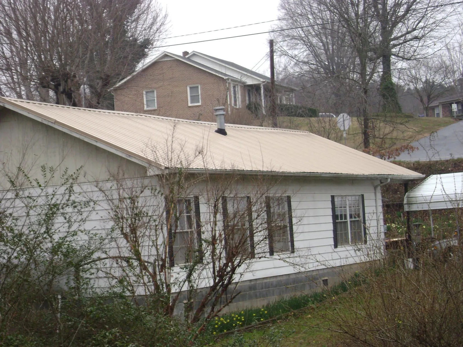 Tan metal roof on a white sided house set into a hillside — Commercial Roofing by Roofing Brothers in Fishers